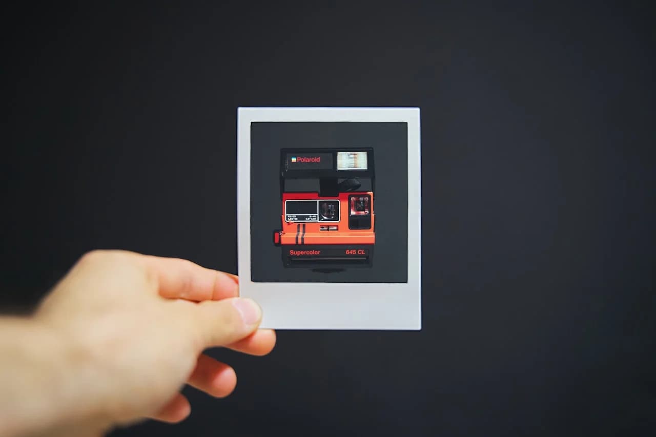 Roka, ki drži manjši fotopapir s sliko polaroidnega fotoaparata