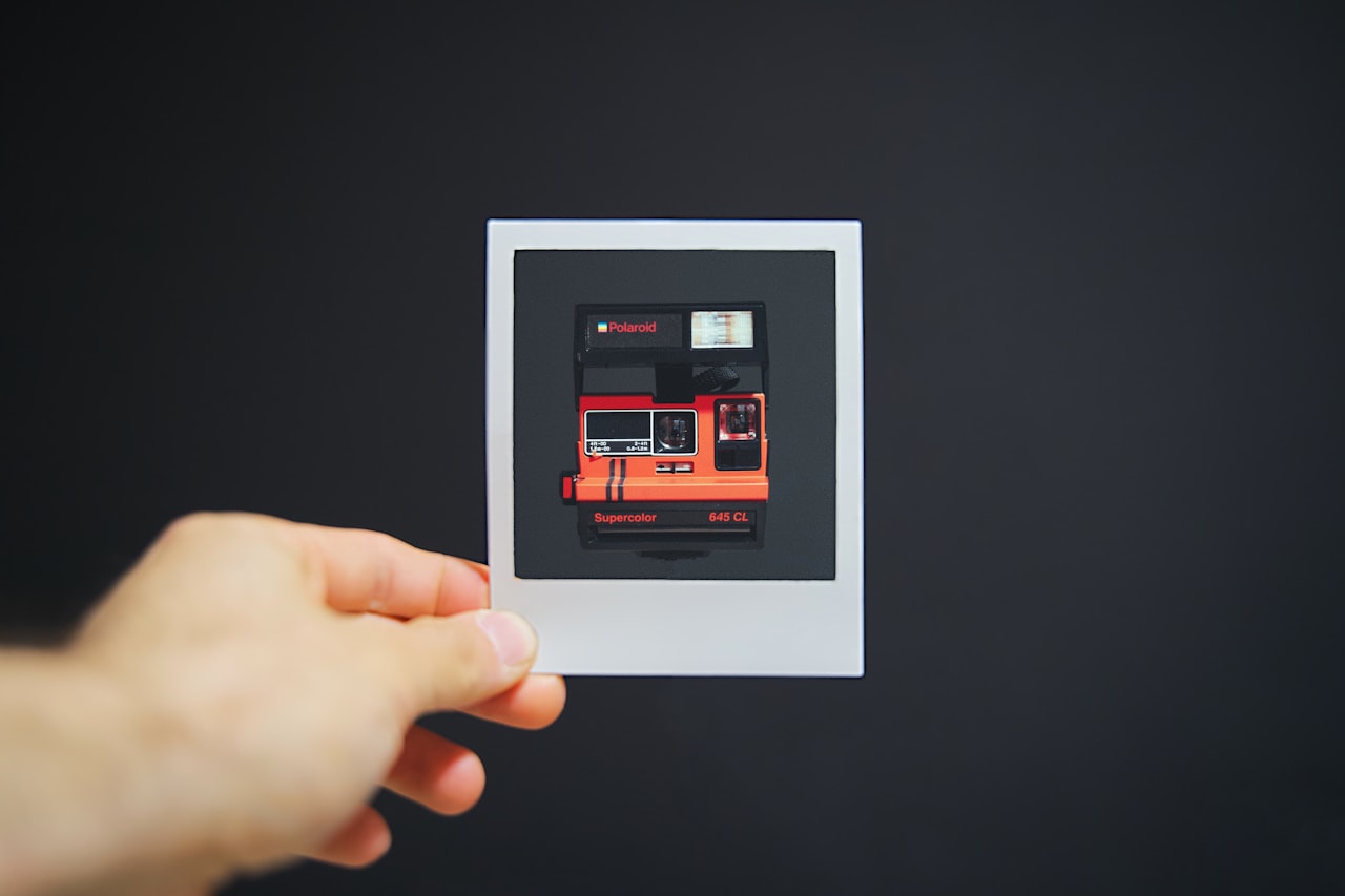 Roka, ki drži manjši fotopapir s sliko polaroidnega fotoaparata