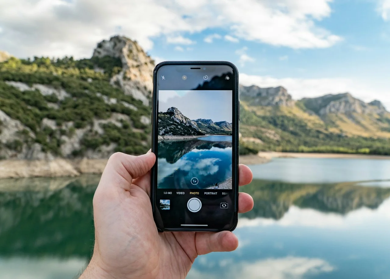 Roka drži telefon, na zaslonu je posnetek jezera in gora