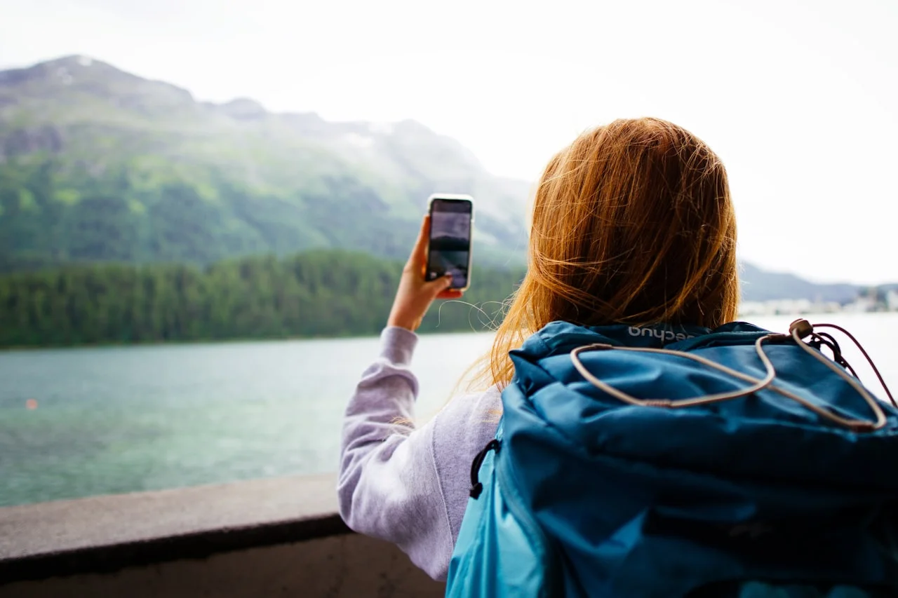 Popotnica z nahrbtnikom s telefonom fotografira gorsko jezero