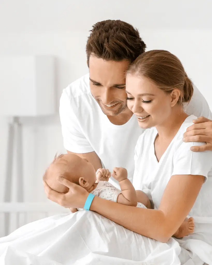 Srečna mlada družina z dojenčkom v postelji - starša v objemu z novorojenčkom