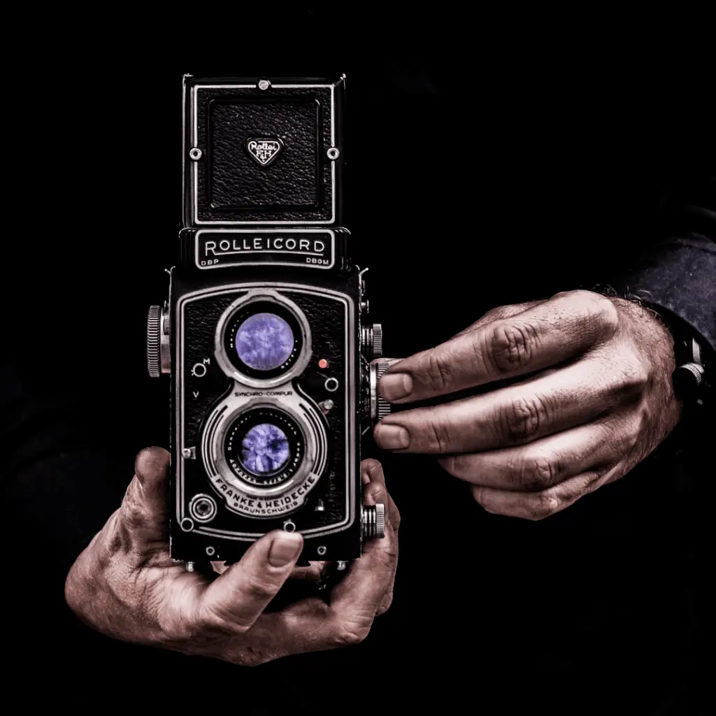 Roke držijo vintage Rolleicord analogni fotoaparat z dvema objektivoma na črnem ozadju